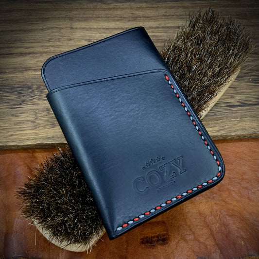 COZY Slim Sleeve Wallet SG Edition in pure black full grain leather with red and white saddle stitching on wooden surface with horsehair brushes