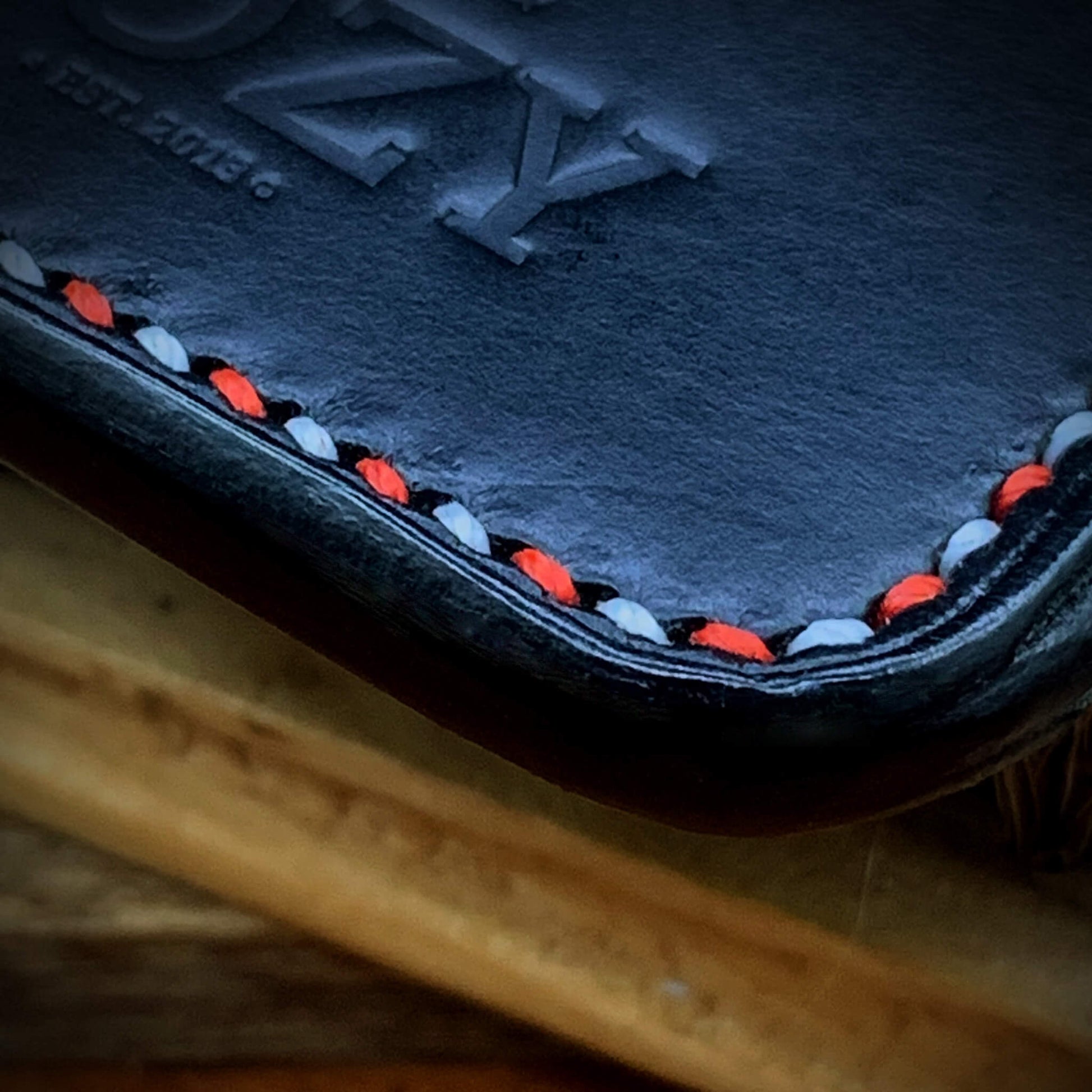 Extreme close-up of alternating red and white hand saddle stitching on COZY Slim Sleeve Wallet SG Edition showing burnished edge detail