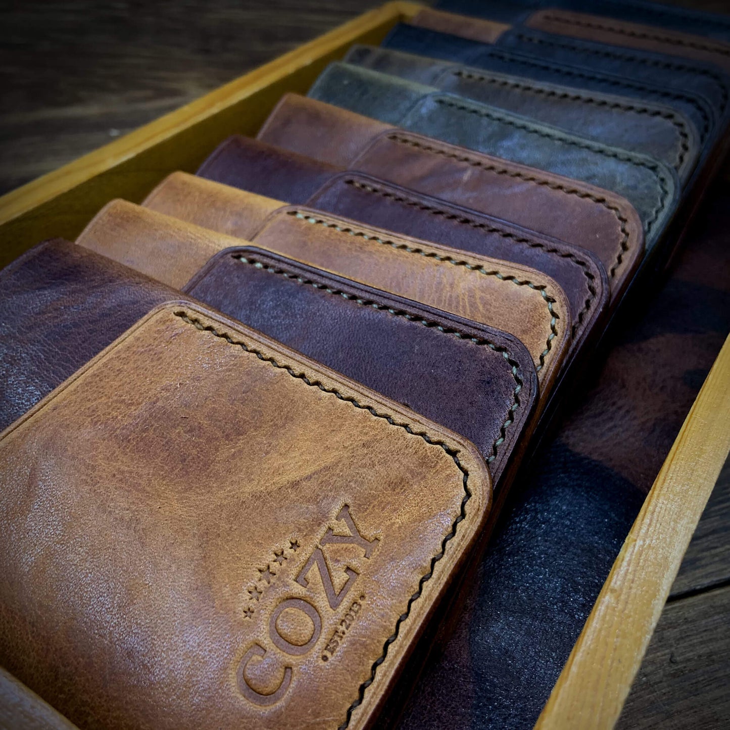 Row of COZY Close-up of the Slim Sleeve Wallet in Italian leather, showcasing the clever folded construction, hand-saddle stitching, and the COZY heritage stamp.