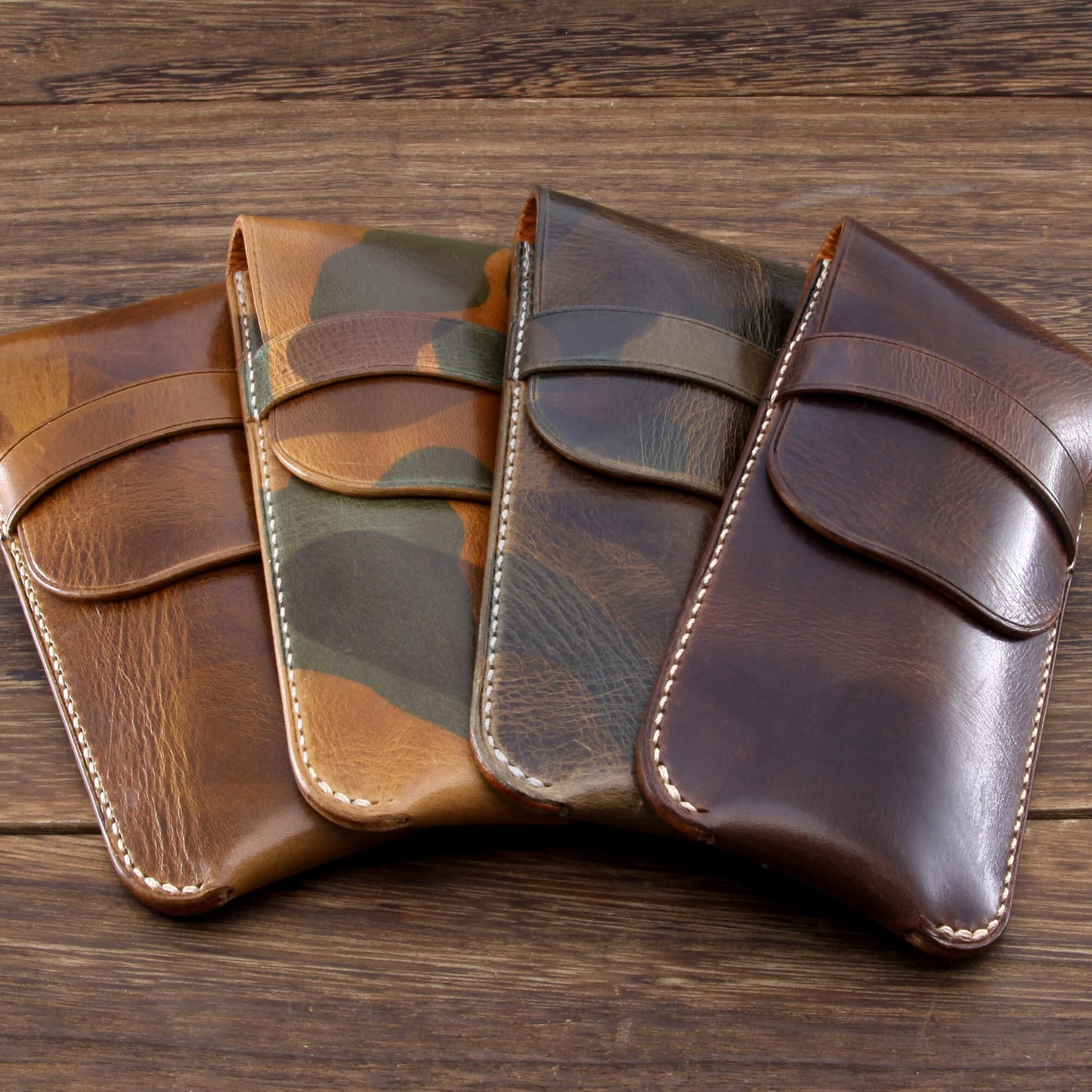Four handcrafted single leather watch travel pouches in tan, camouflage, and dark brown Italian leather, lined up on a wooden table.