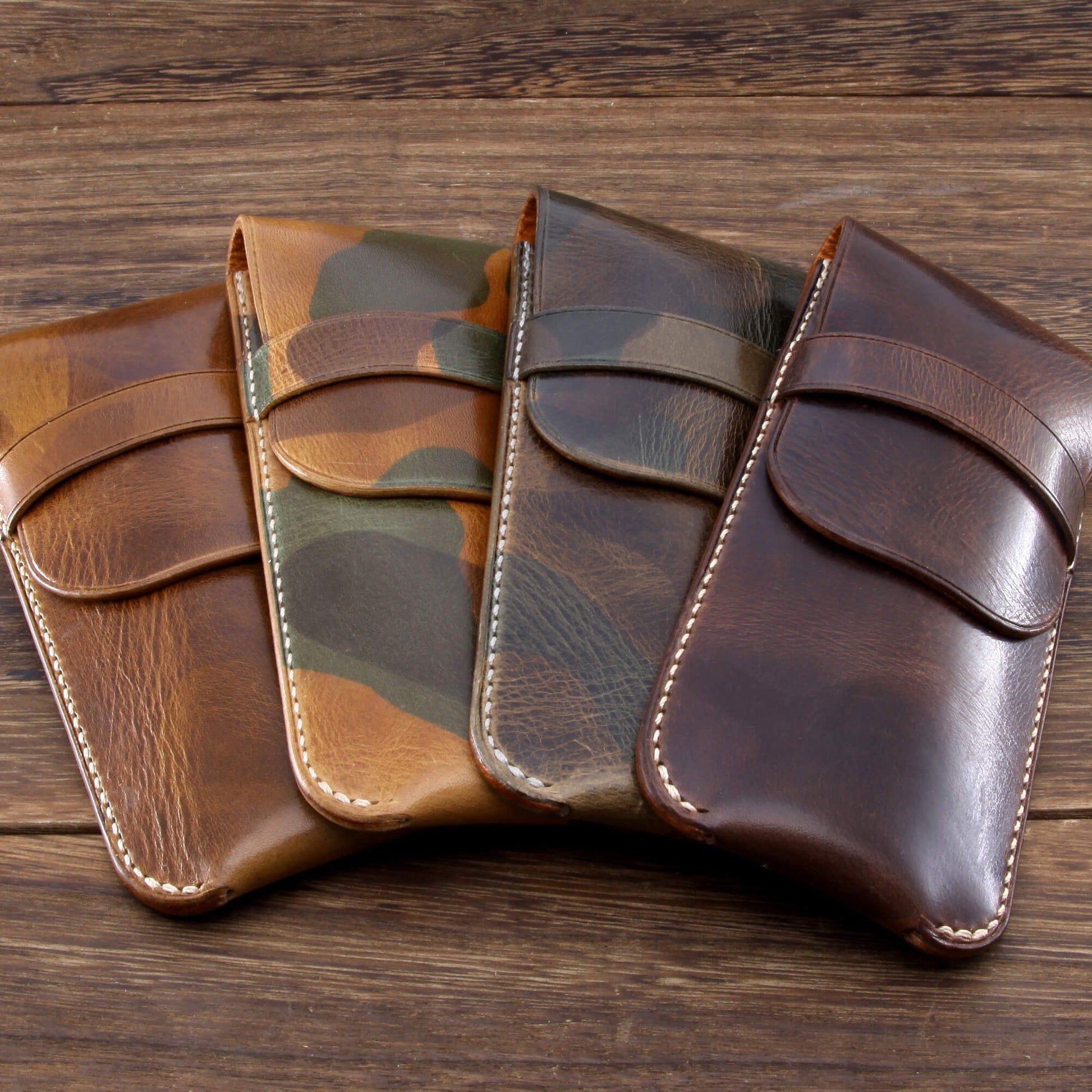 Four handcrafted single leather watch travel pouches in tan, camouflage, and dark brown Italian leather, lined up on a wooden table.
