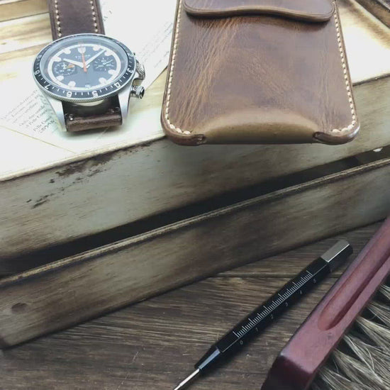 Hands-on showcase of a dark brown leather watch sleeve by Cozy Handmade, demonstrating the secure strap closure and thick protective lining.