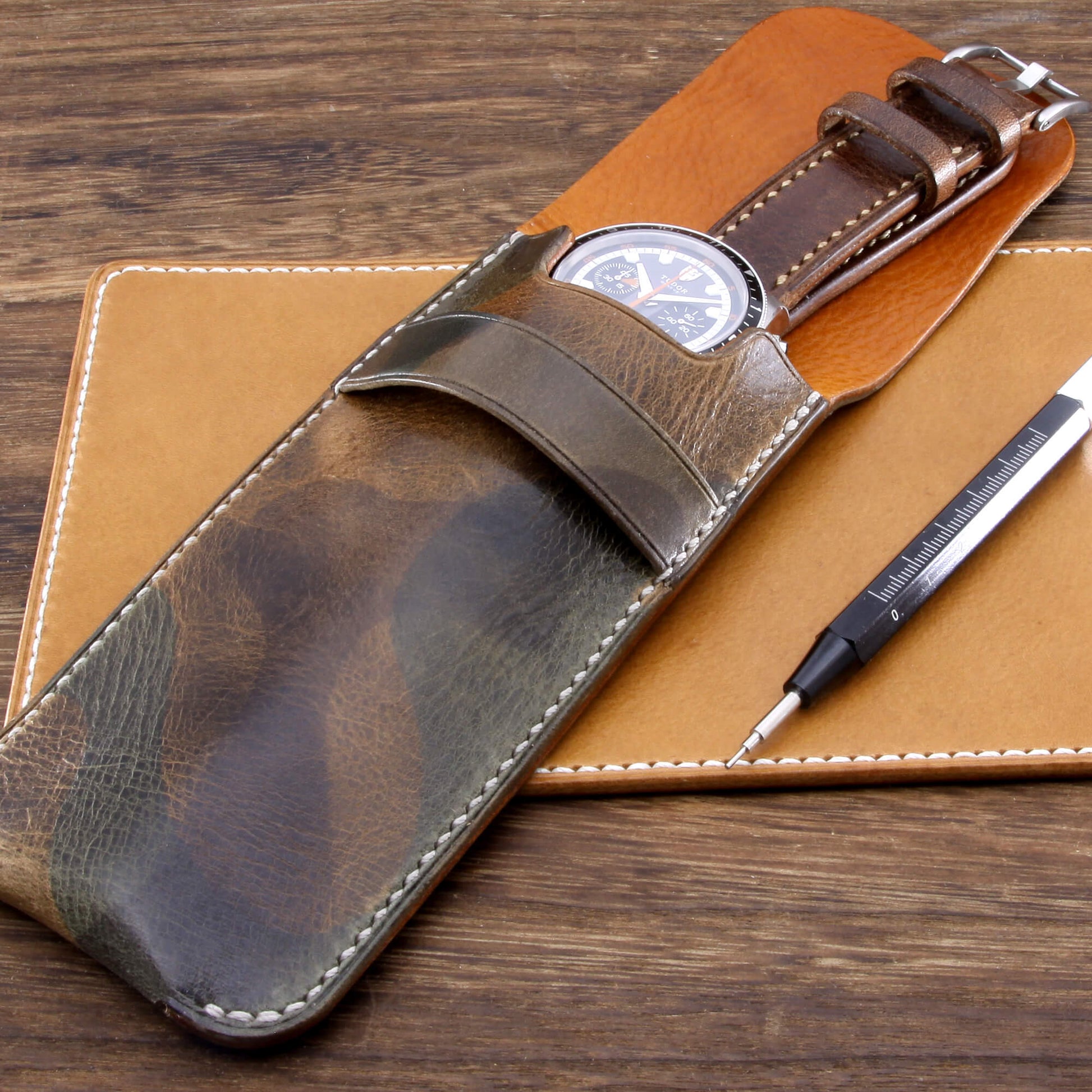 Premium Italian vegetable-tanned leather watch slip case in Military 107 featuring grey contrast stitching, resting on a leather valet and wooden desk. Hand crafted by Cozy Handmade
