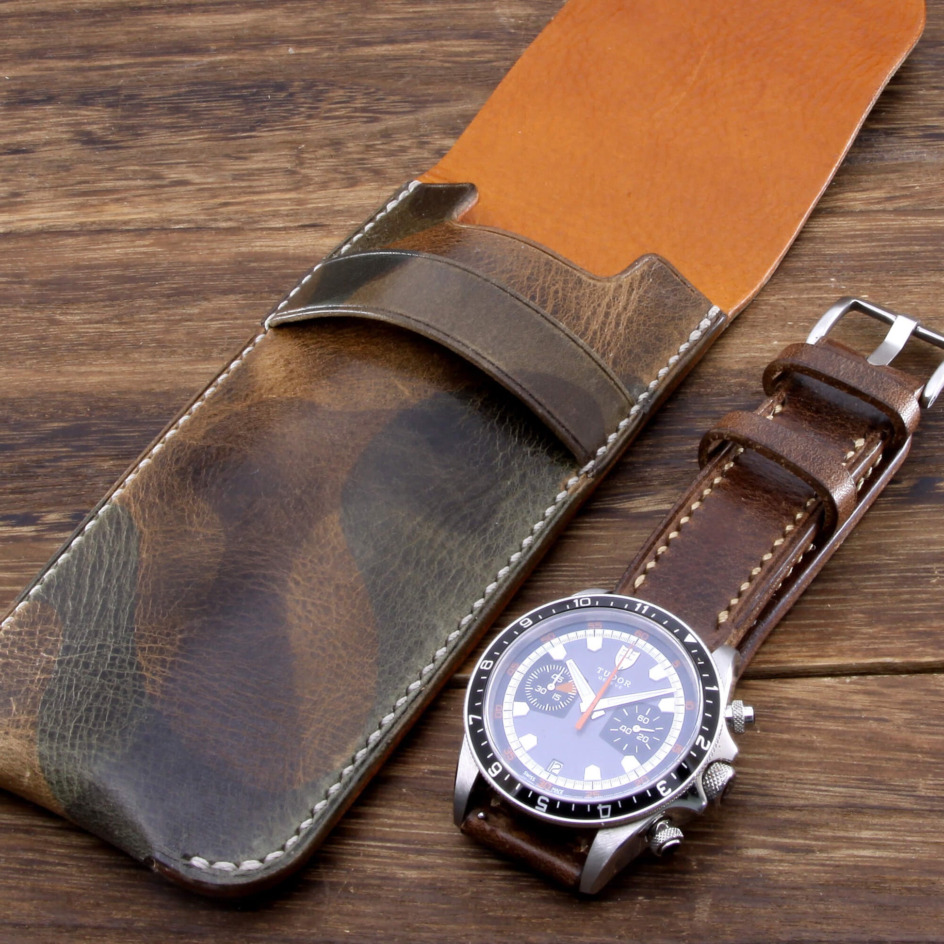 Single watch travel sleeve hand crafted by Cozy Handmade, laying flat on a wooden table next to a luxury chronograph watch.